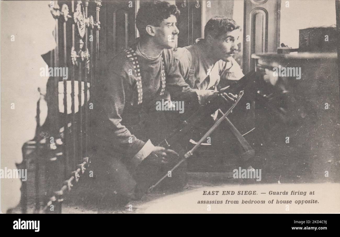 'East End Siege. - Guards firing at assassins from bedroom of house opposite': postcard of the 1911 Siege of Sidney Street, showing soldiers armed with rifles preparing to shoot at the occupants of 100 Sidney Street. They are crouching in front of an iron bedstead Stock Photo
