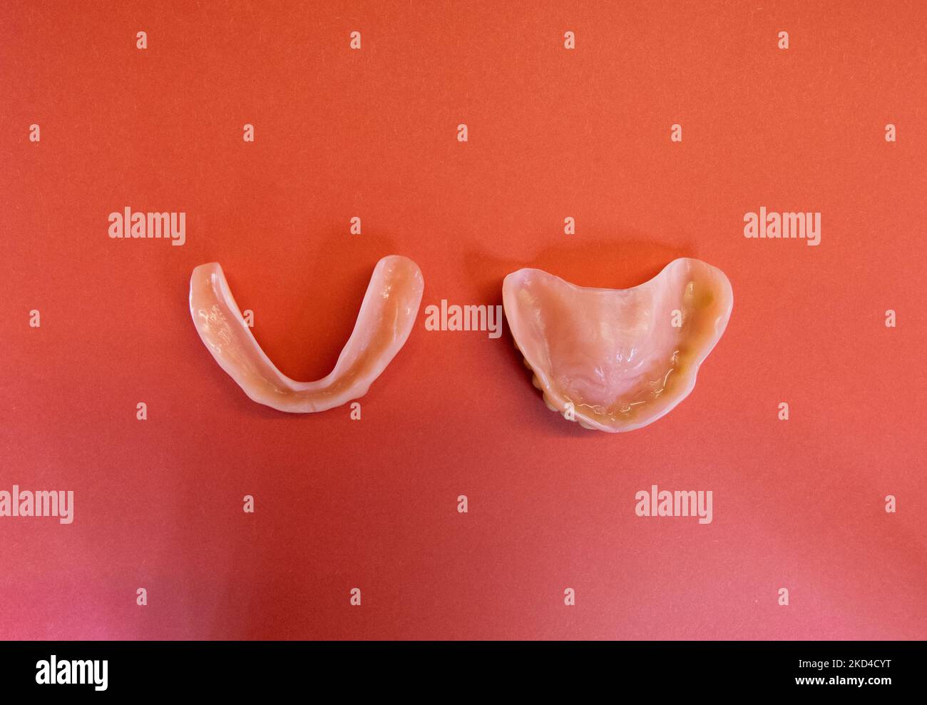 a pair of Dentures (top and bottom) - removable false teeth made of acrylic isolated on a red background - both sets facing down Stock Photo