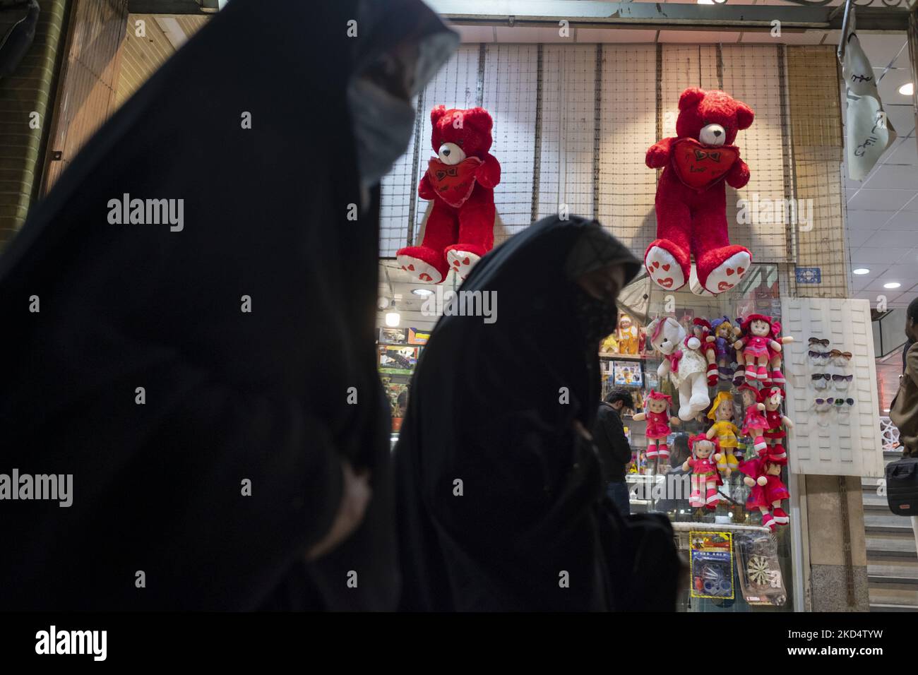 Iranian veiled women walk past two red teddy bears hanged on a wall just out of a toy shop near a holy shrine in the holy city of Qom 145Km (90 miles) south of Tehran on March 10, 2022. (Photo by Morteza Nikoubazl/NurPhoto) Stock Photo