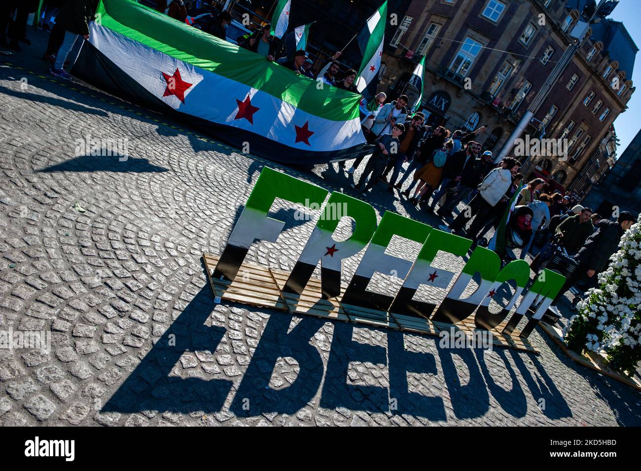 The word FREEDOM with the colors of the Syrian flag is placed in the middle of the square, Syrian people are holding Syrian flags, during a demonstration of the Eleven Years of the Syrian Revolution, organized in Amsterdam, on March 19th, 2022. (Photo by Romy Arroyo Fernandez/NurPhoto) Stock Photo