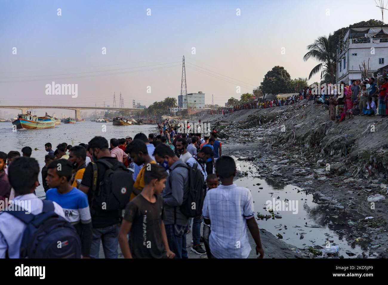 People gather at the bank of Shitalakshya river, where a ferry has sunk after colliding with a sand carrier ship in Narayanganj, Bangladesh on March 20, 2022. Six bodies were recovered, it is not clear immediately how many are still missing. (Photo by Kazi Salahuddin Razu/NurPhoto) Stock Photo