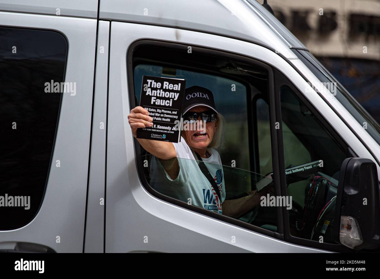 A woman holds a copy of Robert F. Kennedy Jr.'s book 'The Real Anthony Fauci' as a small convoy of truck drivers and people protesting against COVID-19-related mandates drives through Washington, D.C. on March 20, 2022 (Photo by Bryan Olin Dozier/NurPhoto) Stock Photo