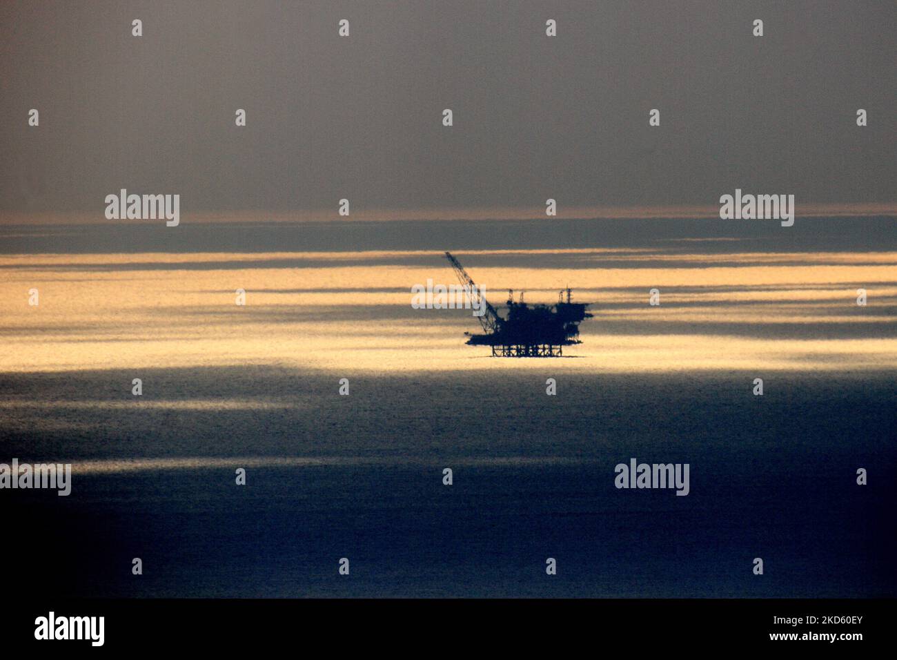 An offshore oil rig platform in the sea with the sunset reflection in ...