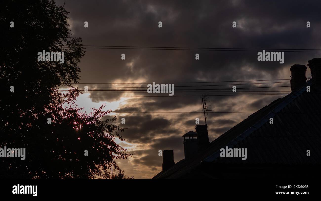 Silhouettes of trees and houses against background of gloomy dark sky Stock Photo