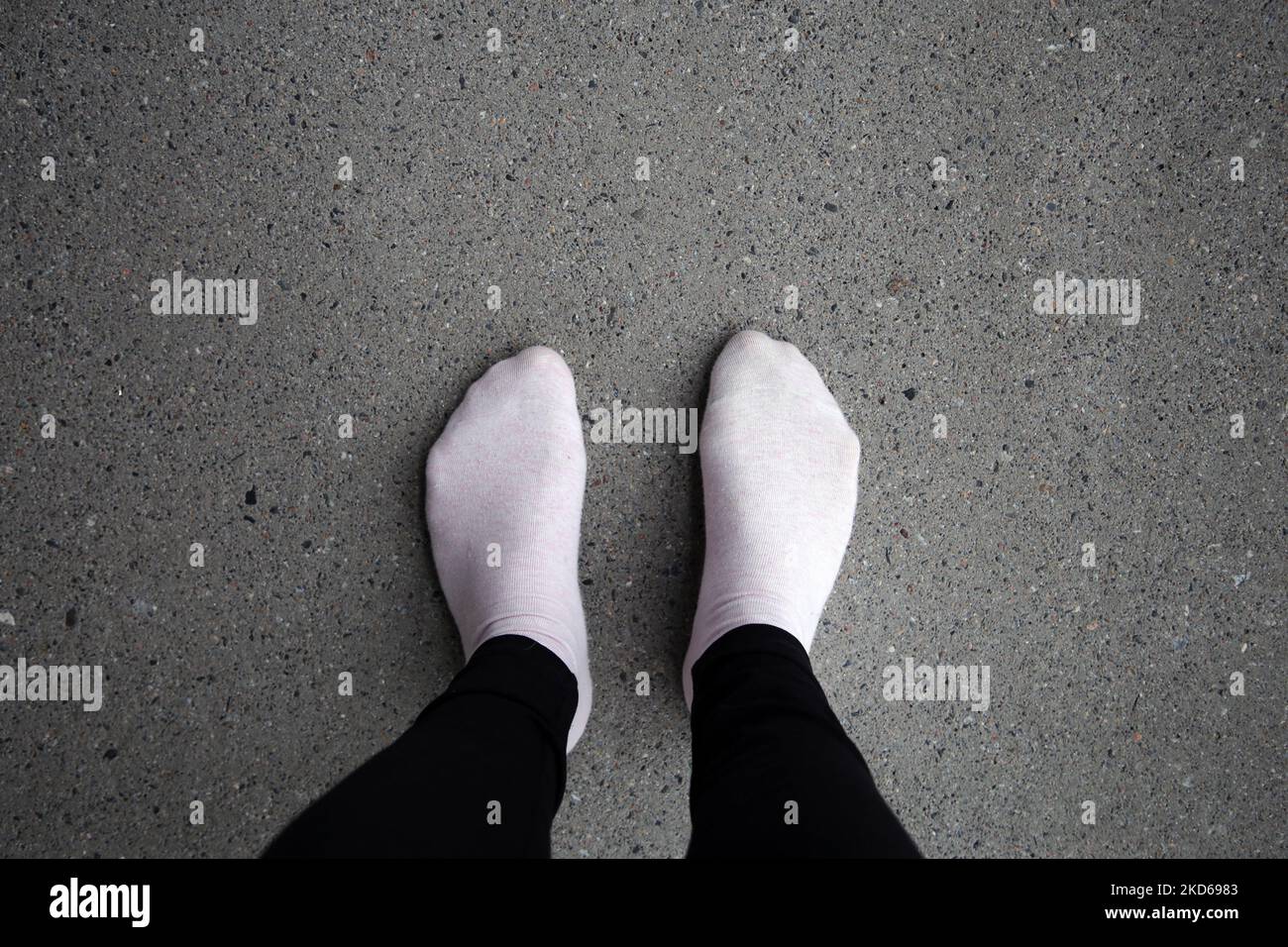 Woman standing on a grey concrete floor while wearing black leggings and pink socks. Color image of unrecognizable person. Stock Photo
