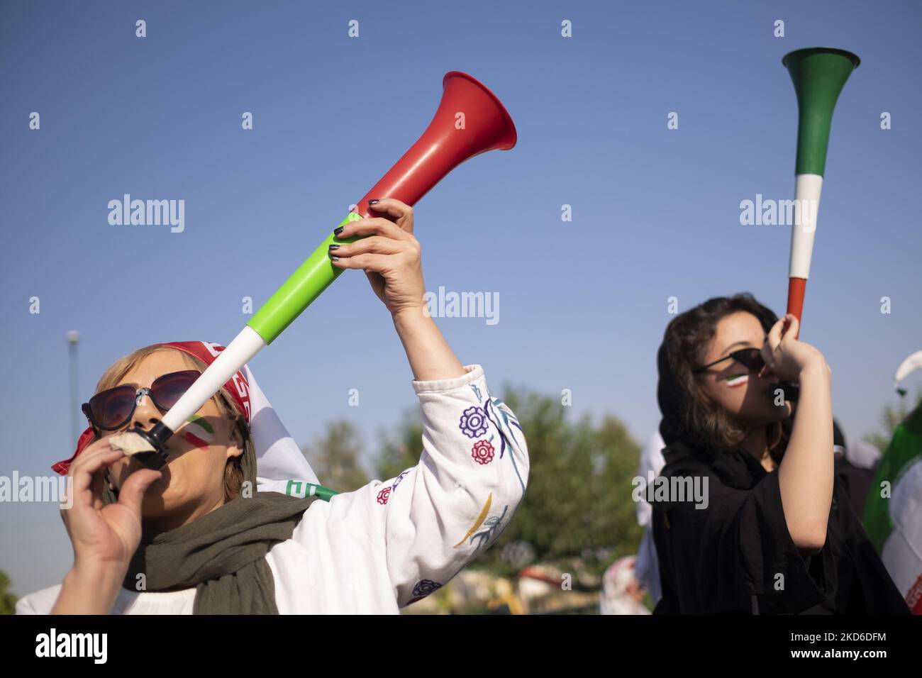 Two Iranian soccer female fans play horns as they wait to enter the