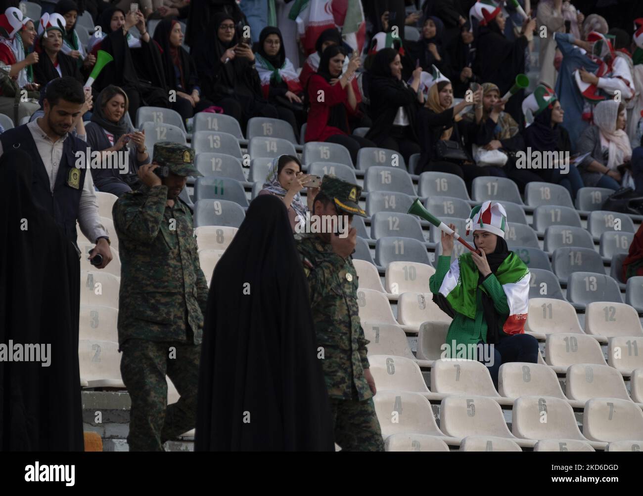 An Iranian soccer female fan plays horn as policemen monitor an area at