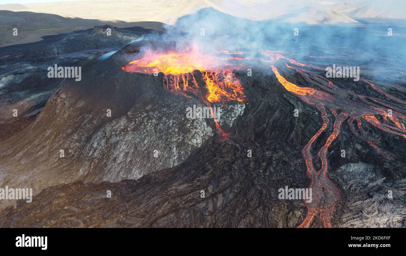 A big erupting volcano with hot lava and smoke coming out of it during the daytime Stock Photo