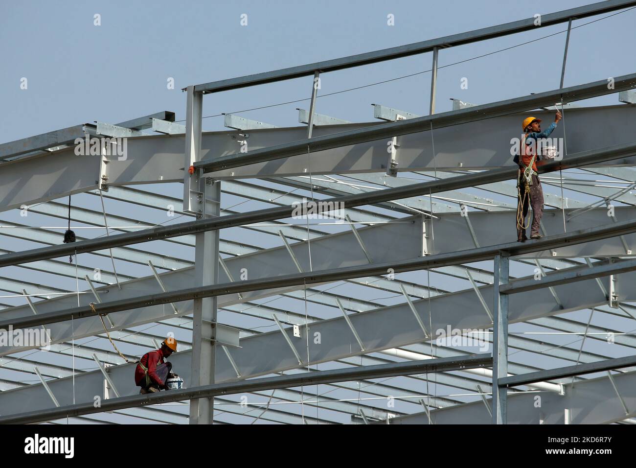 Labourers paint metal girders of an under construction structure on the