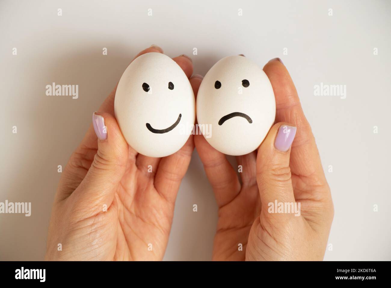 Two eggs with a joyful smile and a sad one in the hands of a girl on a white background, joy and sadness choice, lunch Stock Photo