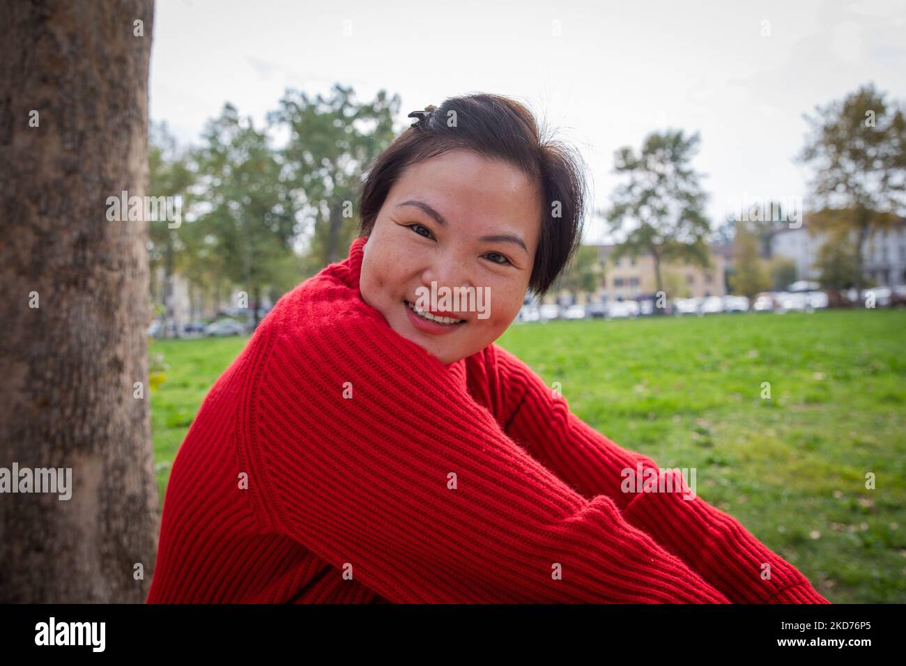 Attractive smiling middle aged chinese woman sitting on the grass at the park. Stock Photo