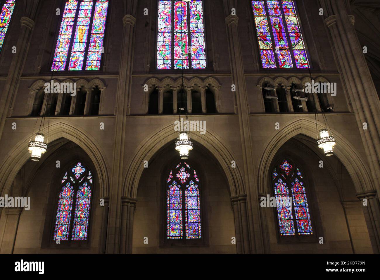 Looking up at six stained glass window on the side of the dimly lit