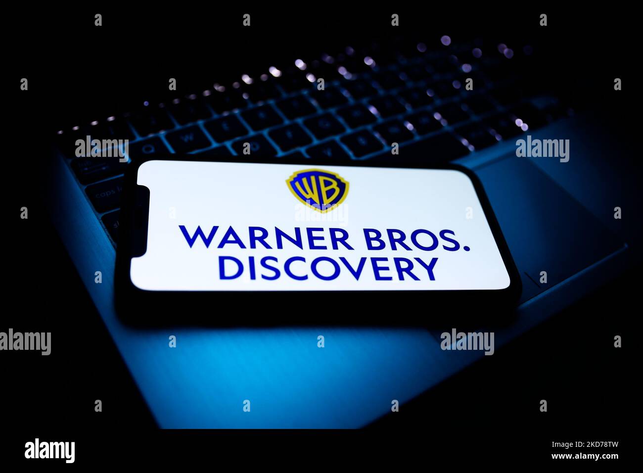 Warner Bros. Discovery logo displayed on a phone screen and a laptop keyboard are seen in this illustration photo taken in Krakow, Poland on April 9, 2022. (Photo by Jakub Porzycki/NurPhoto) Stock Photo