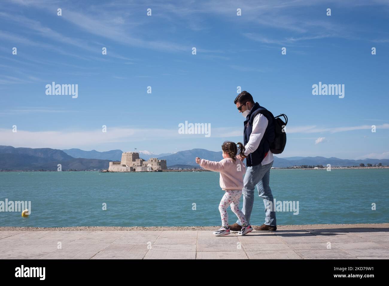 People are walking at the port of Naplion, Greece with Bourtzi island with  Castel da Mar (Sea castle) in the background on April 10, 2022. The fort on  the sea, which has