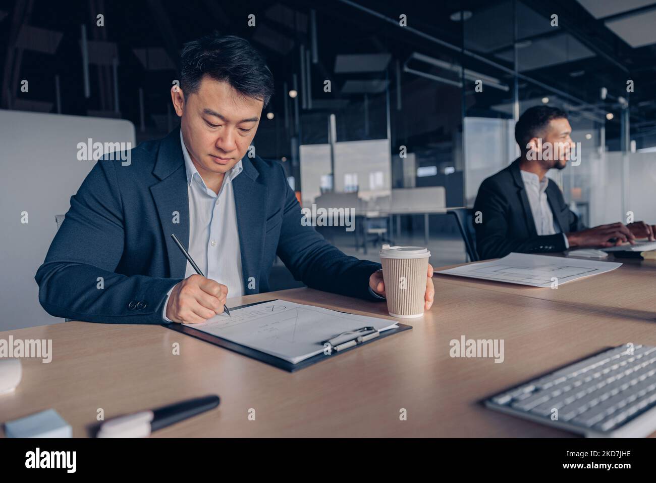 Focused asian businessman drinking coffee while working with documents in modern office Stock Photo