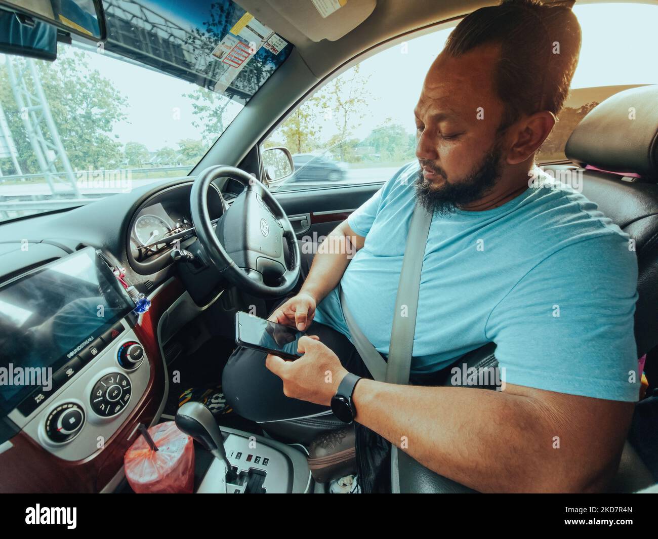 A bearded man using phone while driving a car. Texting while driving. Stock Photo