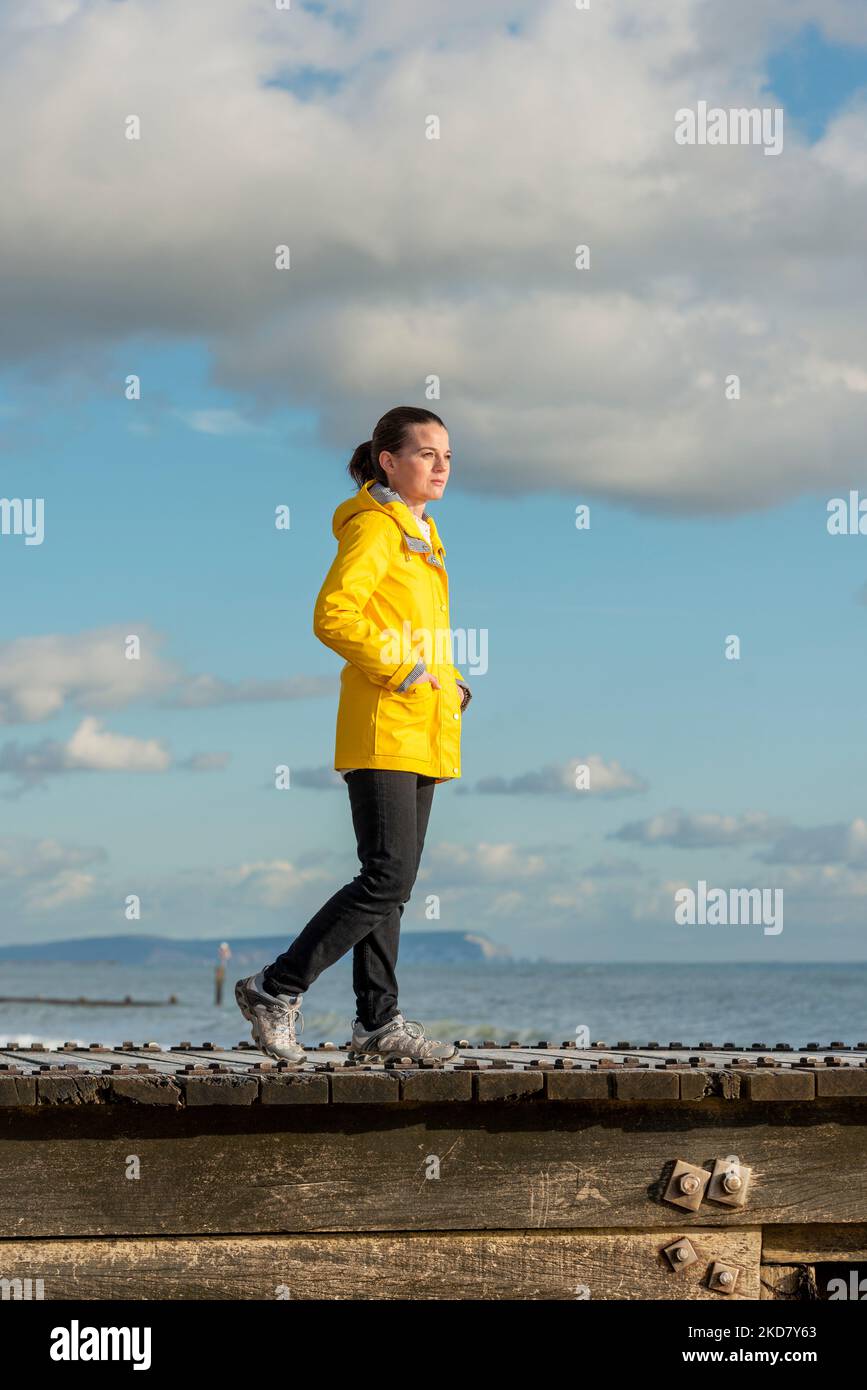 Woman wearing a yellow coat standing by the sea. Concept of freedom, thoughtfulness, mindfulness. Stock Photo