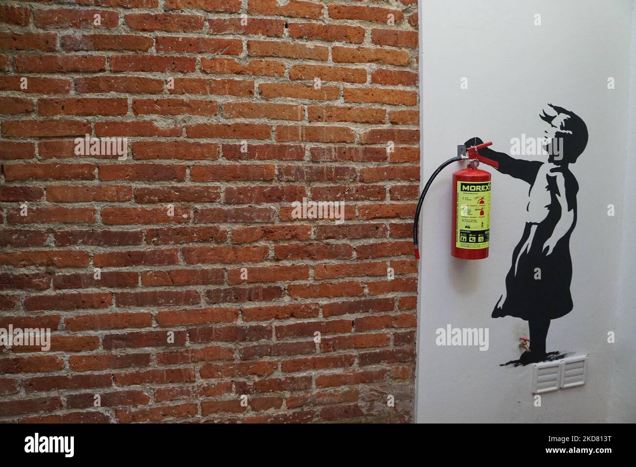 A graffiti of a child carrying the fire extinguisher near a brick wall