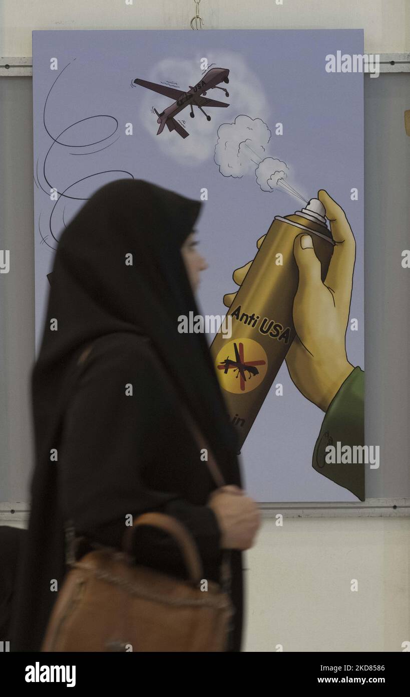 An Iranian veiled woman walks past an anti-U.S. cartoon while visiting the 29th edition of the International Holy Koran Exhibition in the Imam Khomeini Grand mosque in downtown Tehran, during the holy month of Ramadan on April 20, 2022. (Photo by Morteza Nikoubazl/NurPhoto) Stock Photo