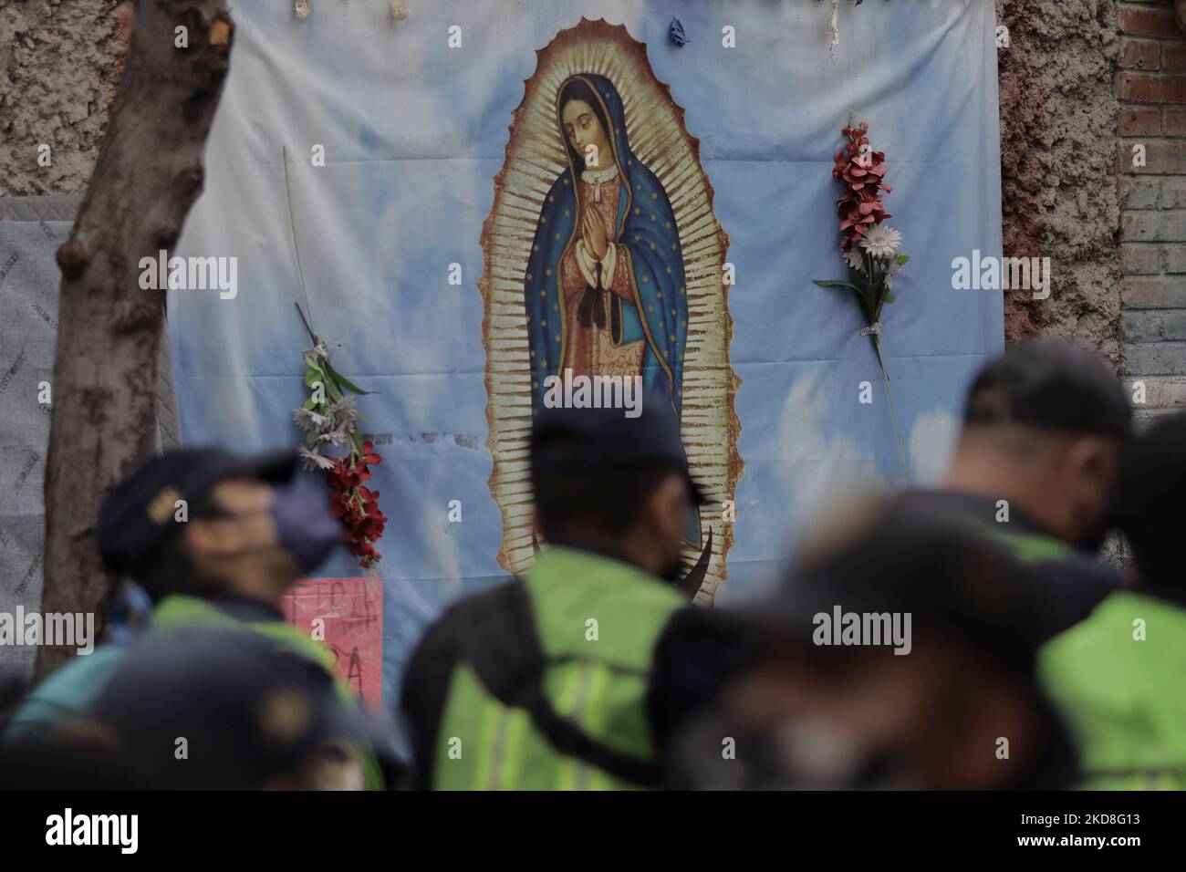 View of an image of the Virgin of Guadalupe while police encapsulate members of the Triqui community of Copala, Oaxaca, after being evicted from an encampment they had maintained for 15 months on Avenida Juárez, Mexico City. After these events, they were once again encapsulated outside a building that gave them refuge for one night in the street of Mapimí and Plomo, in the Valle Gómez neighbourhood. (Photo by Gerardo Vieyra/NurPhoto) Stock Photo