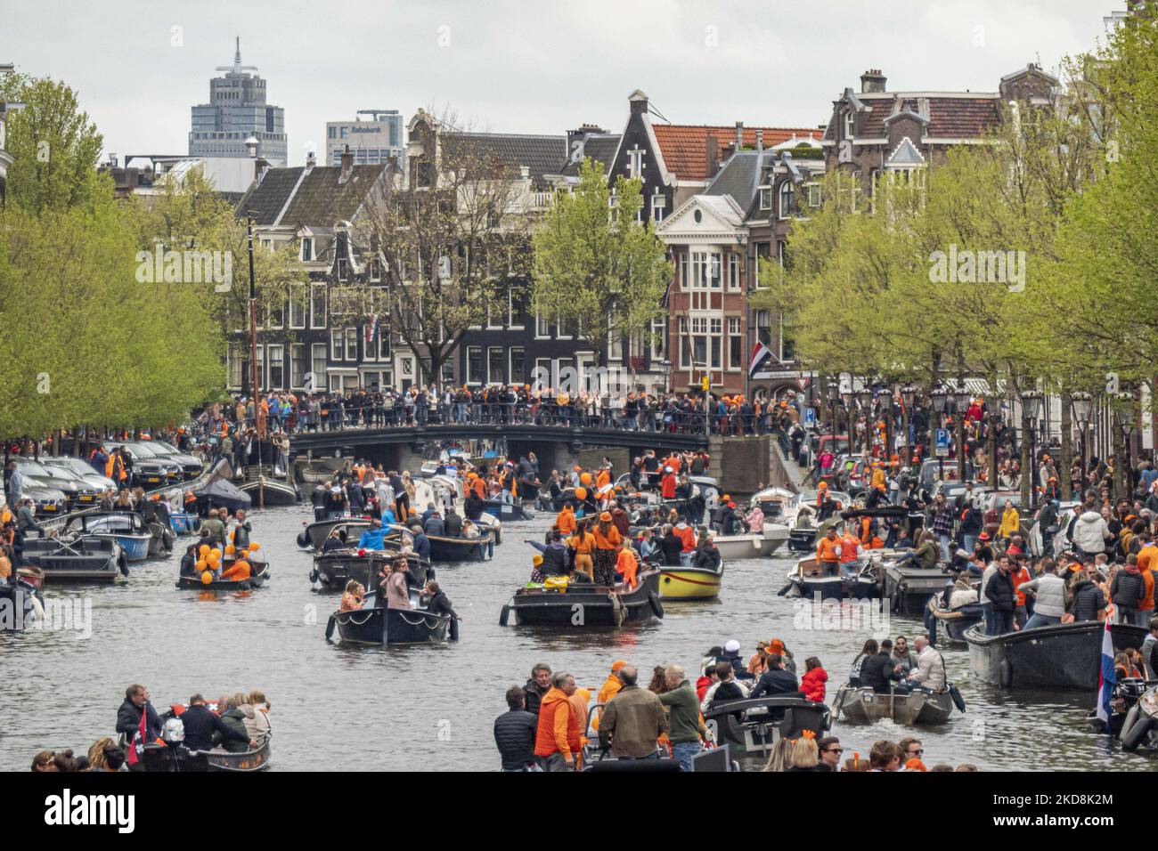 The Netherlands celebrates King's Day after two years of cancellation due to the COVID-19 Coronavirus pandemic and the lockdown restrictions and measures. Thousands of locals and visitors visited the canals of Amsterdam to celebrate with various festivities the birthday of King Willem-Alexander known as Koningsdag, a Dutch national holiday. All kind of boats and vessels are seen in the canals passing under the famous bridges and near the narrow houses of Amsterdam with people on the dancing and having fun. The boats parade down in the inner city canals while travelers gather on the streets. Du Stock Photo