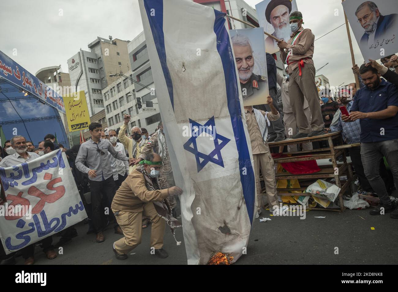 An Iranian demonstrator burns an Israeli flag as the other demonstrators hold portraits of the former commander of Iran’s Islamic Revolutionary Guard Corps’ (IRGC) Quds Force, General Qasem Soleimani (C), Iranian Nuclear scientist, Mohsen Fakhrizadeh (R), and Iran’s Late Leader Ayatollah Ruhollah Khomeini in downtown Tehran during a rally commemorating the International Quds Day, also known as the Jerusalem day, on April 29, 2022. (Photo by Morteza Nikoubazl/NurPhoto) Stock Photo