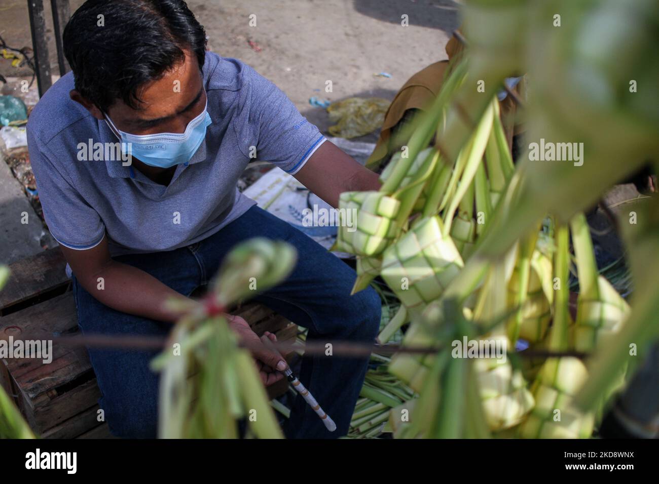 A trader weaves coconut leaves used to make traditional rice cakes called 'Ketupat' preparations ahead of Eid al-Fitr, at a traditional market in Lhokseumawe, On May 1, 2022, Indonesia. (Photo by Fachrul Reza/NurPhoto) Stock Photo