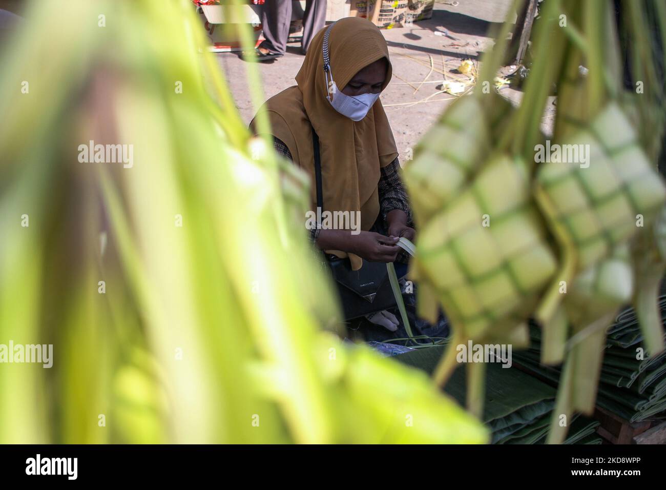 A trader weaves coconut leaves used to make traditional rice cakes called 'Ketupat' preparations ahead of Eid al-Fitr, at a traditional market in Lhokseumawe, On May 1, 2022, Indonesia. (Photo by Fachrul Reza/NurPhoto) Stock Photo