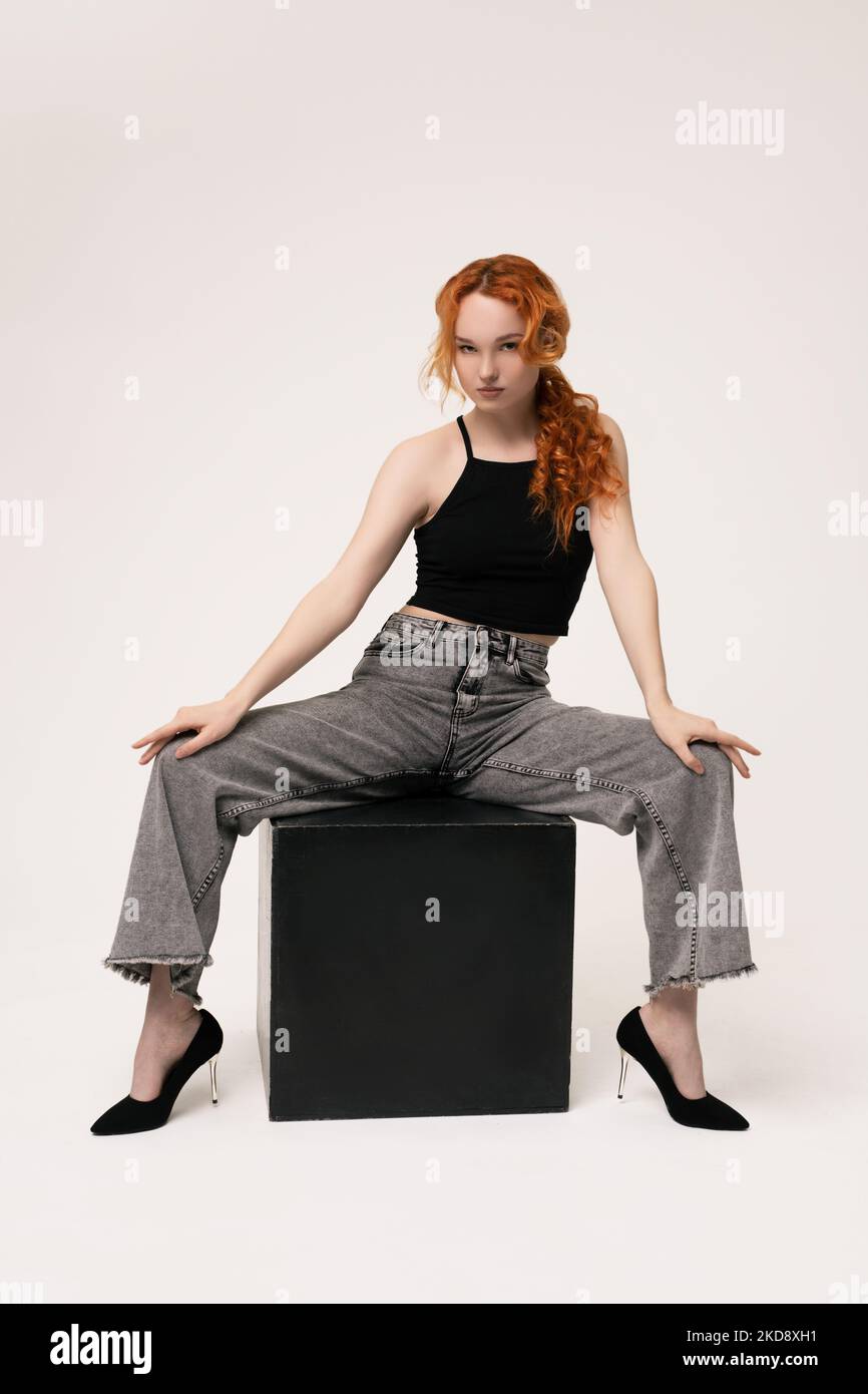 Confident young lady sitting on cube and looking at camera Stock Photo