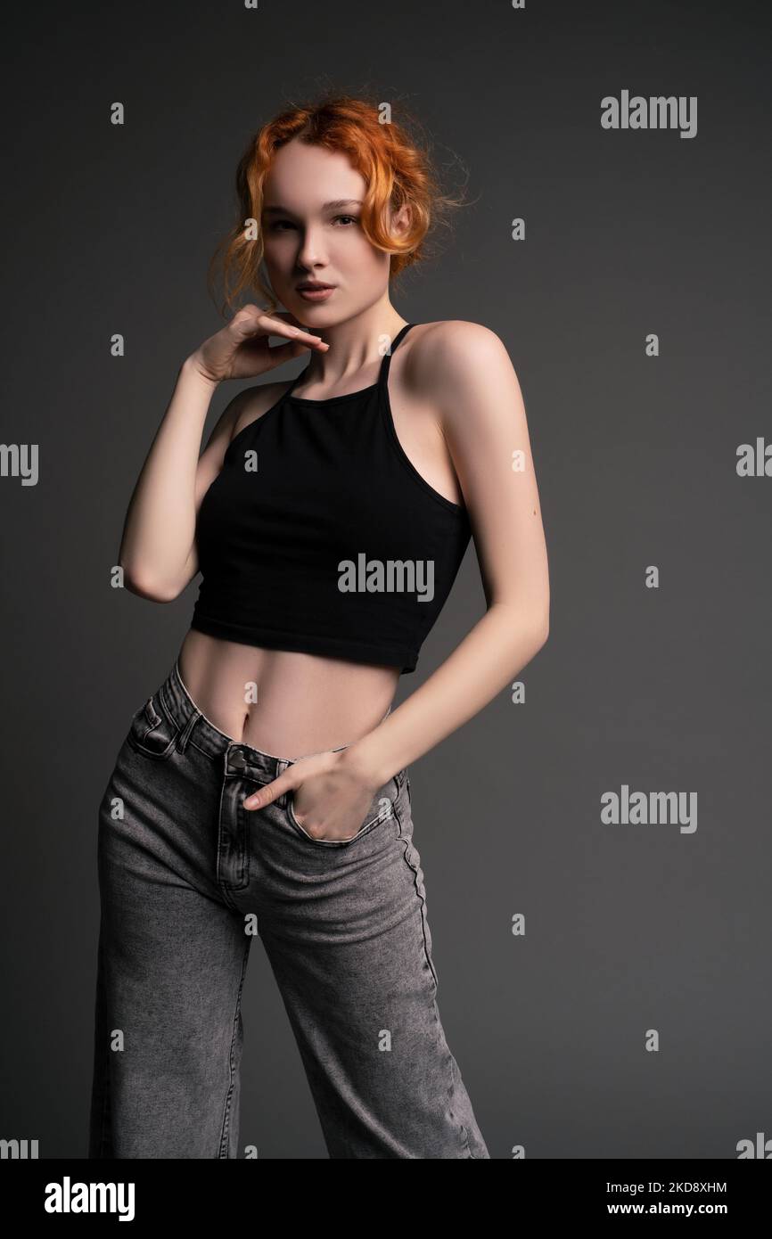 Confident young woman standing in gray studio with hand on waist Stock Photo