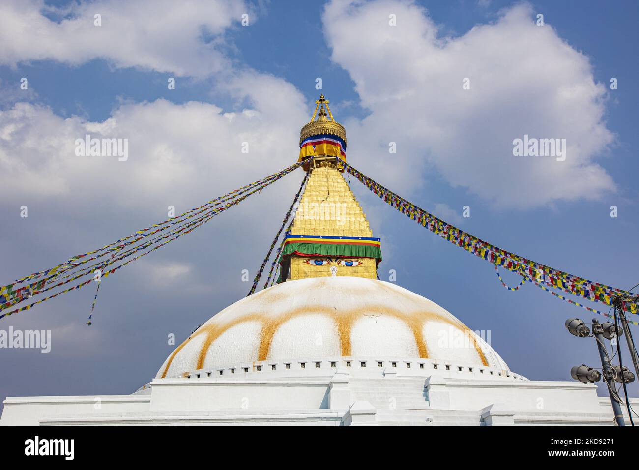 Closeup at the golden top with the Eyes of the stupa, where the praying flags begin. Boudhanath or Bouddha Stupa in Kathmandu a UNESCO World Heritage Site and a legendary place for the Newar and Tibetan Buddhist mythology with the golden part having the Eyes of Boudhanath and the praying flags. One of the most popular tourist attraction in Kathmandu, the mandala makes it one of the largest spherical stupas in Nepal and the world. The Stupa was damaged in the 2015 April earthquake. The Stupa is located on the ancient trade route from Tibet, and the Tibetan Refugees after the 1950s decided to li Stock Photo