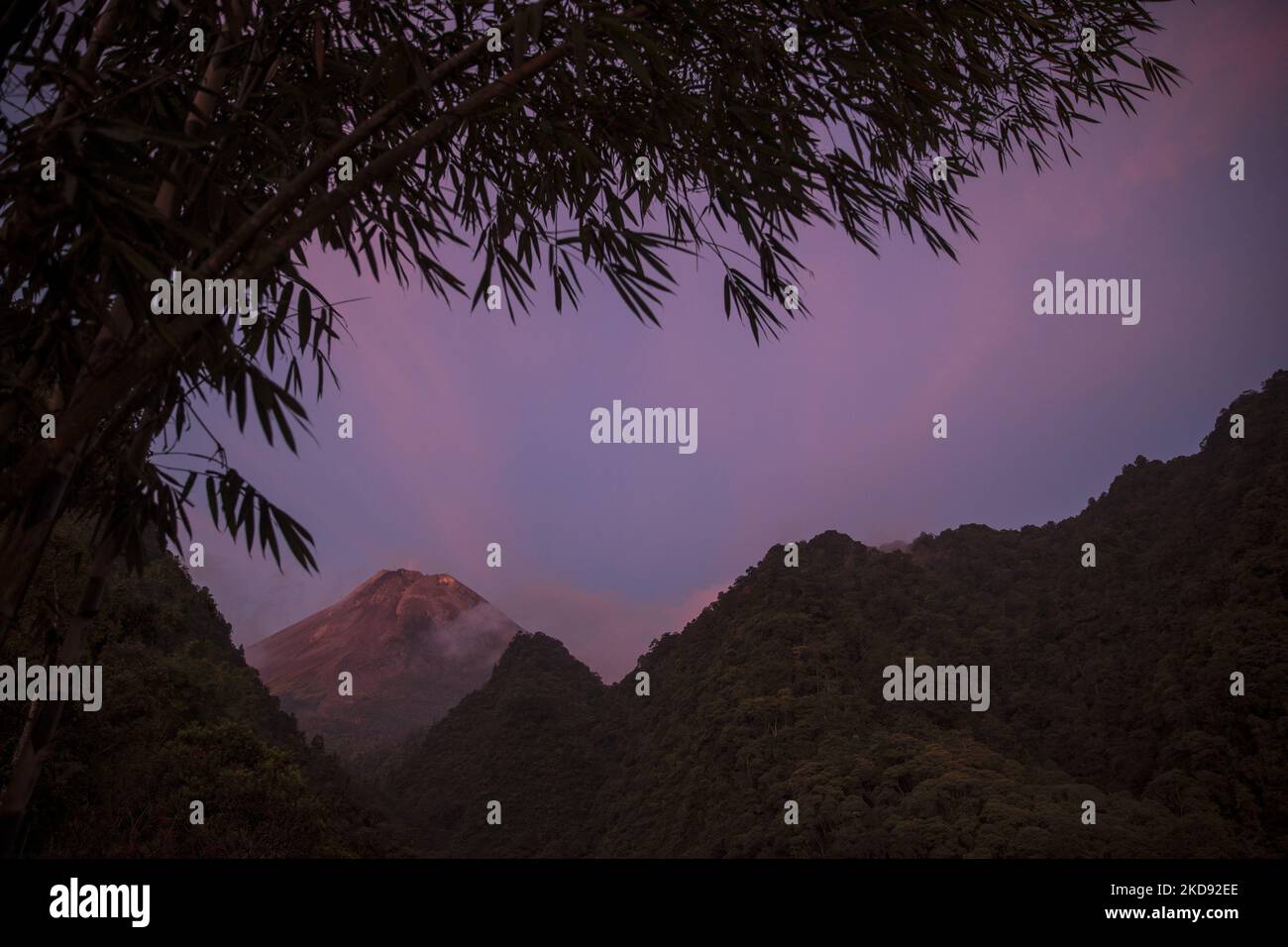 The scenery of Mount Merapi volcano by sunset is seen from Turgo village, Sleman district in Yogyakarta, Indonesia on January 3, 2022. Merapi is located in one of the most densely populated parts of Java with over 11,000 people living on the slopes of the mountain. Mount Merapi, measuring 2,968 metres high, is known as one of the most active volcanoes in Indonesia, with an eruption occurring every two to five years. (Photo by Garry Lotulung/NurPhoto) Stock Photo
