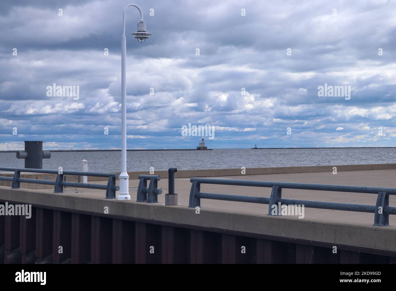 White light post on a paved boat dock with lighthouse in the background