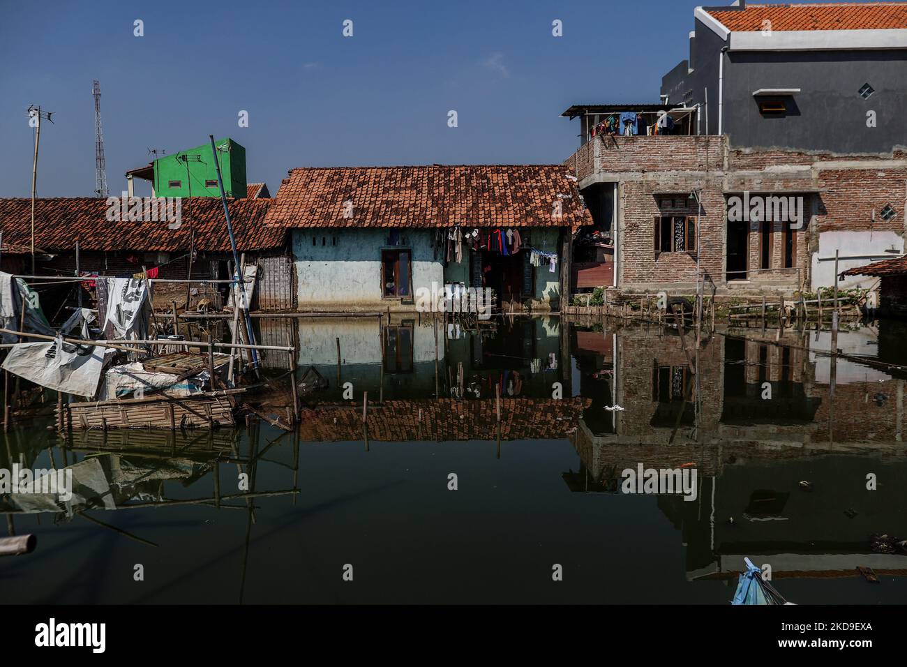 Homes surrounded by rising sea levels is seen at low-lying Jeruk Sari neighborhood in coastal Pekalongan, Central Java, Indonesia, June 5, 2021. An area in which almost every available space is used for batik production, with a high level of poverty, vulnerable to both rising sea levels and high river peak flows. They hangs and washes at a polluted river for process traditional Javanese textile called Batik. Batik is a traditional Indonesian method of using wax to resist water-based dyes to depict patterns and drawings on fabric. At the heart of the problem is Pekalongan’s overreliance on grou Stock Photo