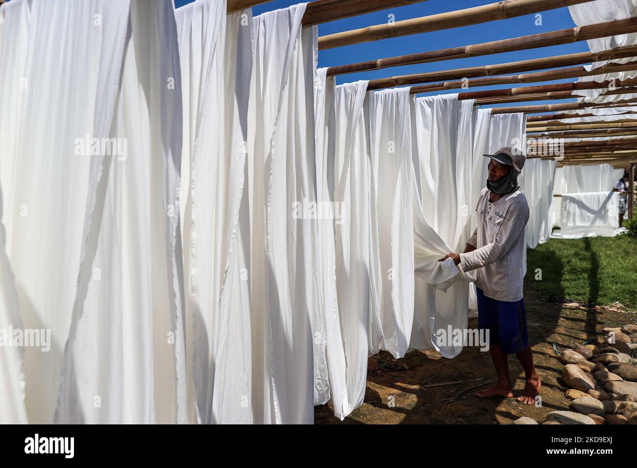 A worker hangs a cloth to dry out on the sun beside homes surrounded by rising sea levels at low-lying Jeruk Sari neighborhood in coastal Pekalongan, Central Java, Indonesia, June 5, 2021. An area in which almost every available space is used for batik production, with a high level of poverty, vulnerable to both rising sea levels and high river peak flows. They hangs and washes at a polluted river for process traditional Javanese textile called Batik. Batik is a traditional Indonesian method of using wax to resist water-based dyes to depict patterns and drawings on fabric. At the heart of the  Stock Photo