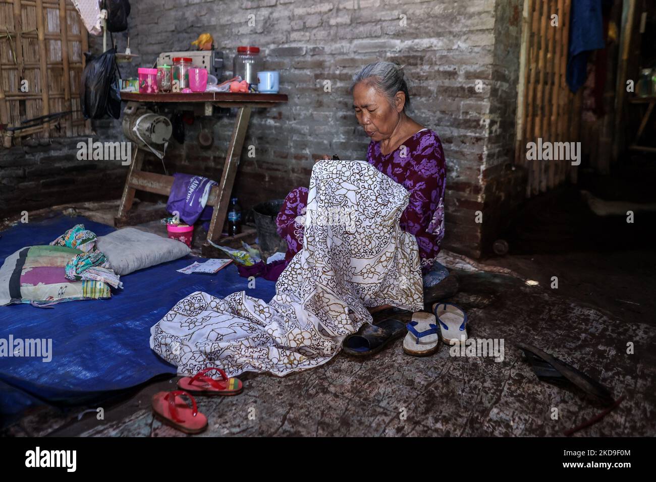 A batik craftswoman applies melted wax using a spouted tool called a canting as make traditional Javanese textile called batik at low-lying Jeruk Sari neighborhood in coastal Pekalongan, Central Java, Indonesia, June 5, 2021. An area in which almost every available space is used for batik production, with a high level of poverty, vulnerable to both rising sea levels and high river peak flows. Pekalongan is a city known for batik, a traditional Indonesian method of using wax to resist water-based dyes to depict patterns and drawings, usually on fabric. This textile has traditionally been crafte Stock Photo