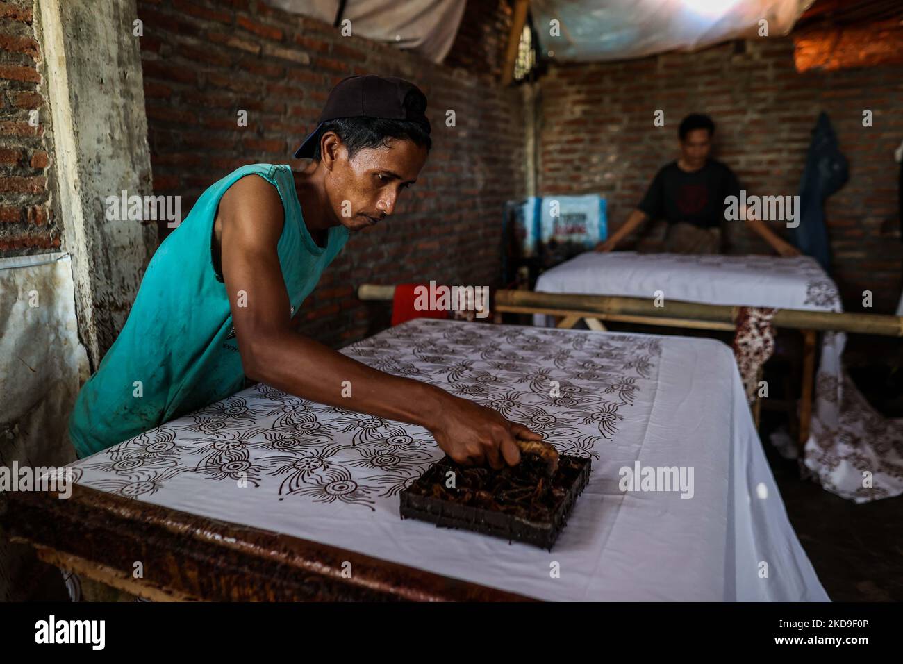 A worker uses copper stamps to imprint patterns onto traditional Javanese textile called batik at low-lying Jeruk Sari neighborhood in coastal Pekalongan, Central Java, Indonesia, June 5, 2021. An area in which almost every available space is used for batik production, with a high level of poverty, vulnerable to both rising sea levels and high river peak flows. Pekalongan is a city known for batik, a traditional Indonesian method of using wax to resist water-based dyes to depict patterns and drawings, usually on fabric. This textile has traditionally been crafted by hand in family workshops an Stock Photo