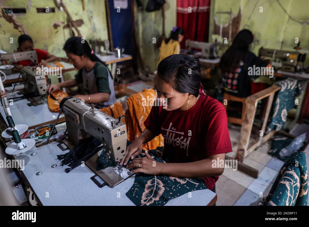 Workers sew batik clothing products traditional Javanese textile called batik at low-lying Jeruk Sari neighborhood in coastal Pekalongan, Central Java, Indonesia, June 5, 2021. An area in which almost every available space is used for batik production, with a high level of poverty, vulnerable to both rising sea levels and high river peak flows. Pekalongan is a city known for batik, a traditional Indonesian method of using wax to resist water-based dyes to depict patterns and drawings, usually on fabric. This textile has traditionally been crafted by hand in family workshops and small-scale cot Stock Photo
