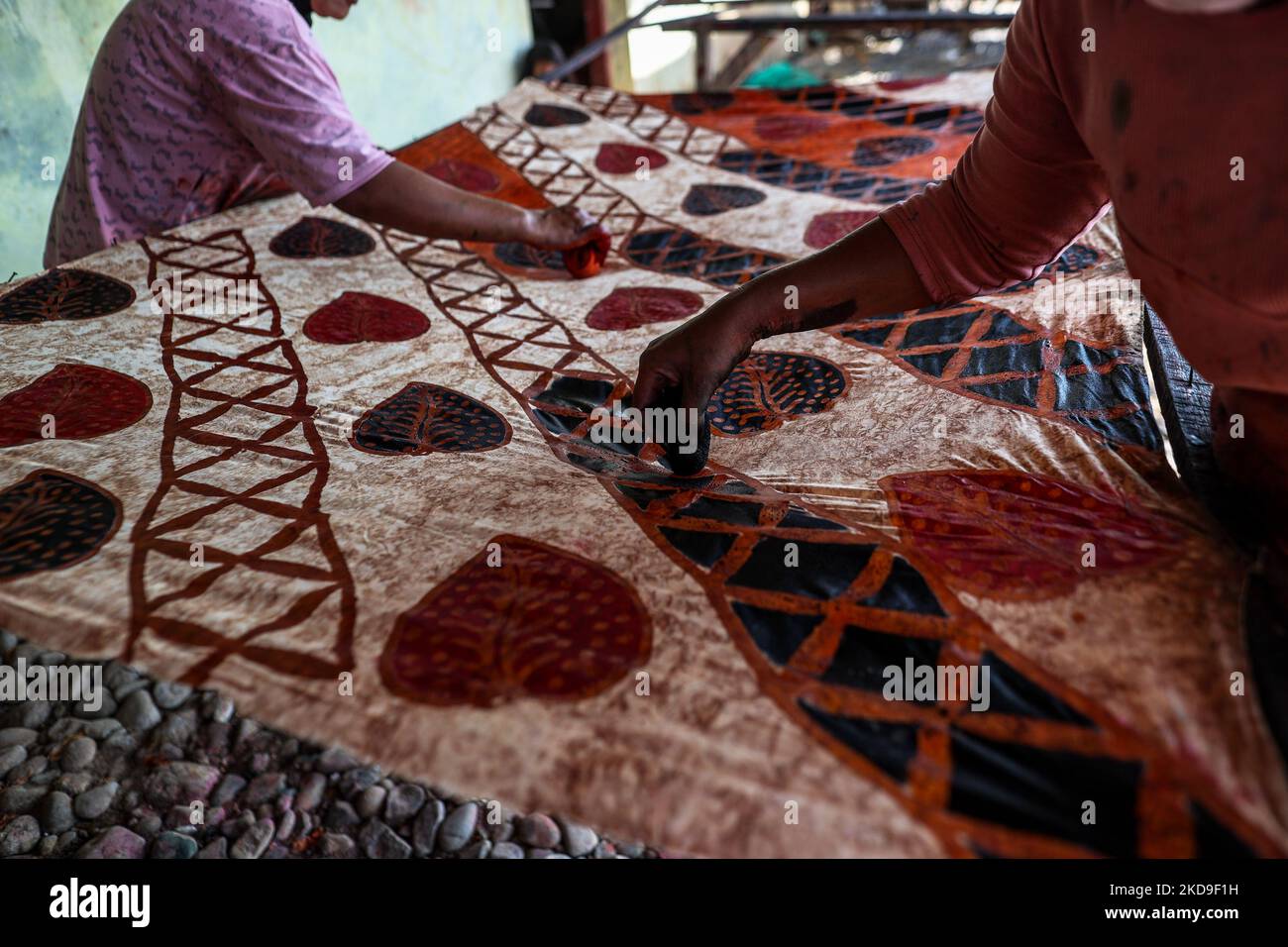 Workers making batik cloth pattern with a wax-resist cloth dyeing technique onto traditional Javanese textile called batik at low-lying Jeruk Sari neighborhood in coastal Pekalongan, Central Java, Indonesia, June 5, 2021. An area in which almost every available space is used for batik production, with a high level of poverty, vulnerable to both rising sea levels and high river peak flows. Pekalongan is a city known for batik, a traditional Indonesian method of using wax to resist water-based dyes to depict patterns and drawings, usually on fabric. This textile has traditionally been crafted by Stock Photo
