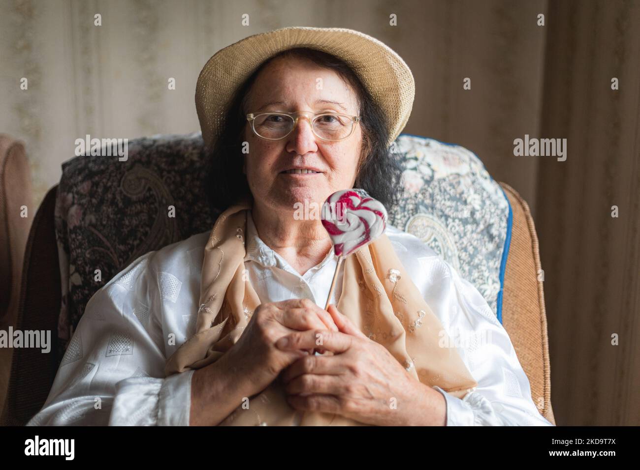 Elderly woman holding a candy lollipop, sitting in a chair Stock Photo