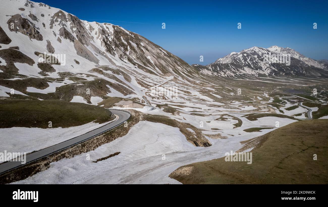 A drone view of a road with snow on the ridges in Campo Imperatore in the Gran Sasso and Laga Mountains National Park, on May 13, 2022. -Gran Sasso d'Italia is a massif in the Apennine Mountains of Italy. Its highest peak, Corno Grande (2,912 metres), is the highest mountain in the Apennines, and the second-highest mountain in Italy outside the Alps. (Photo by Manuel Romano/NurPhoto) Stock Photo