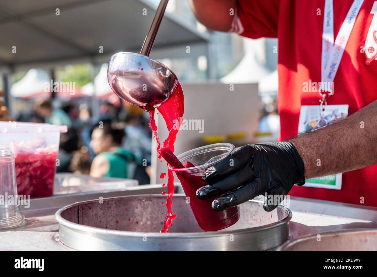 A man is filling fermented red carrot juice into a plastic glass in a traditional food festival in Turkey country, close up Stock Photo