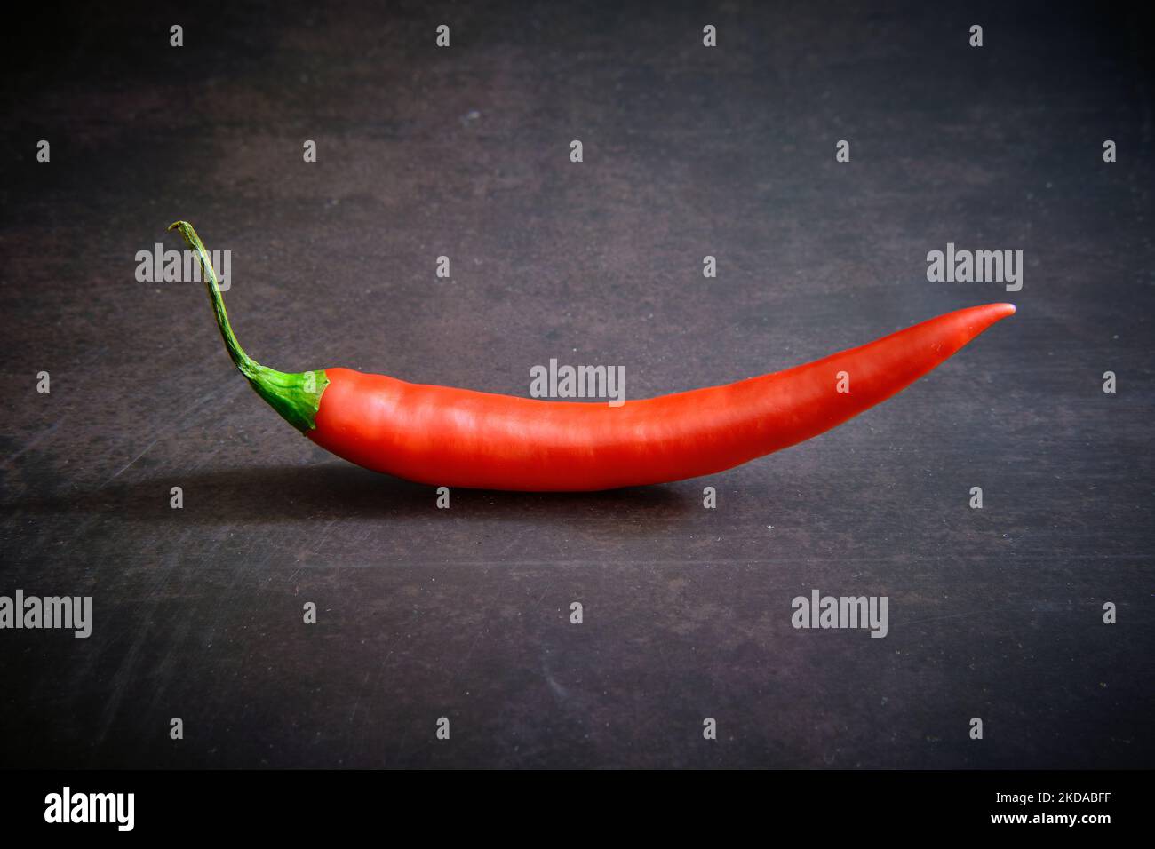 A close-up of a red fresh chilli pepper isolated on a dark background ...