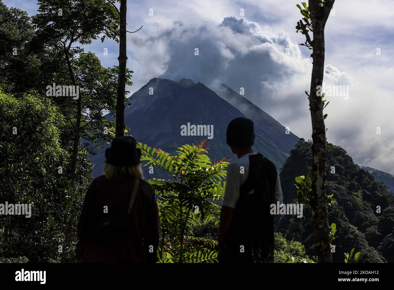 Farmers look at Mount Merapi as it erupts several times as seen from Turgo village, Sleman district in Yogyakarta, Indonesia on May 13, 2022. Merapi is located in one of the most densely populated parts of Java with over 11,000 people living on the slopes of the mountain. Mount Merapi, measuring 2,968 metres high, is known as one of the most active volcanoes in Indonesia, with an eruption occurring every two to five years. (Photo by Garry Lotulung/NurPhoto) Stock Photo