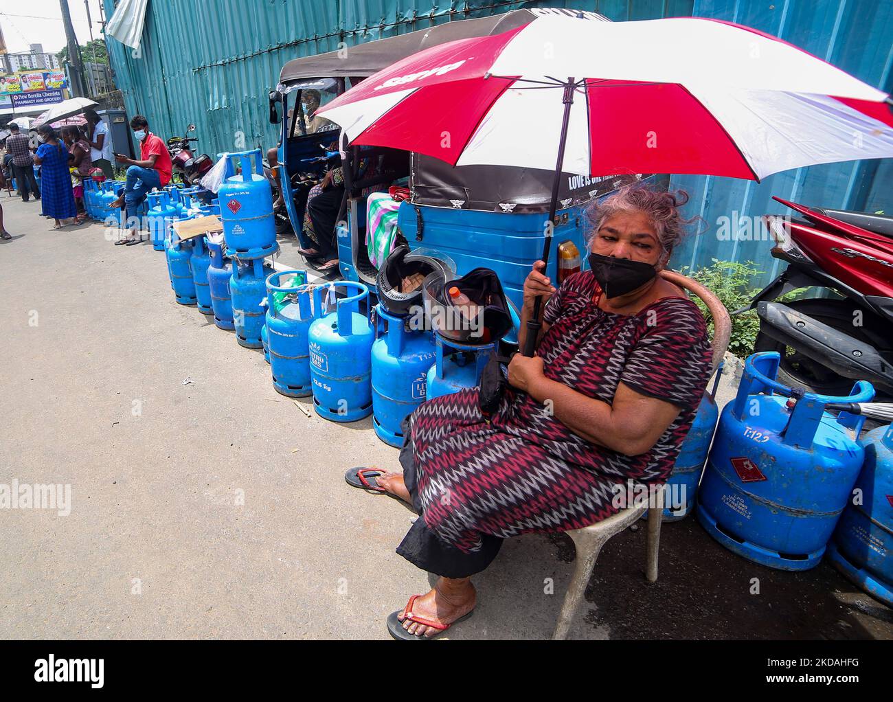 A Sri Lankan woman sits on a chair and wait in line with empty cooking