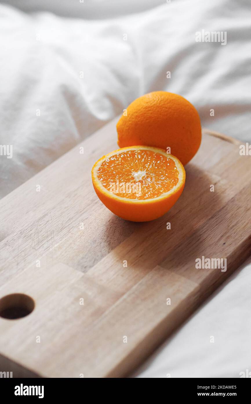 A vertical shot of a sliced orange on a wooden board on white fabric ...