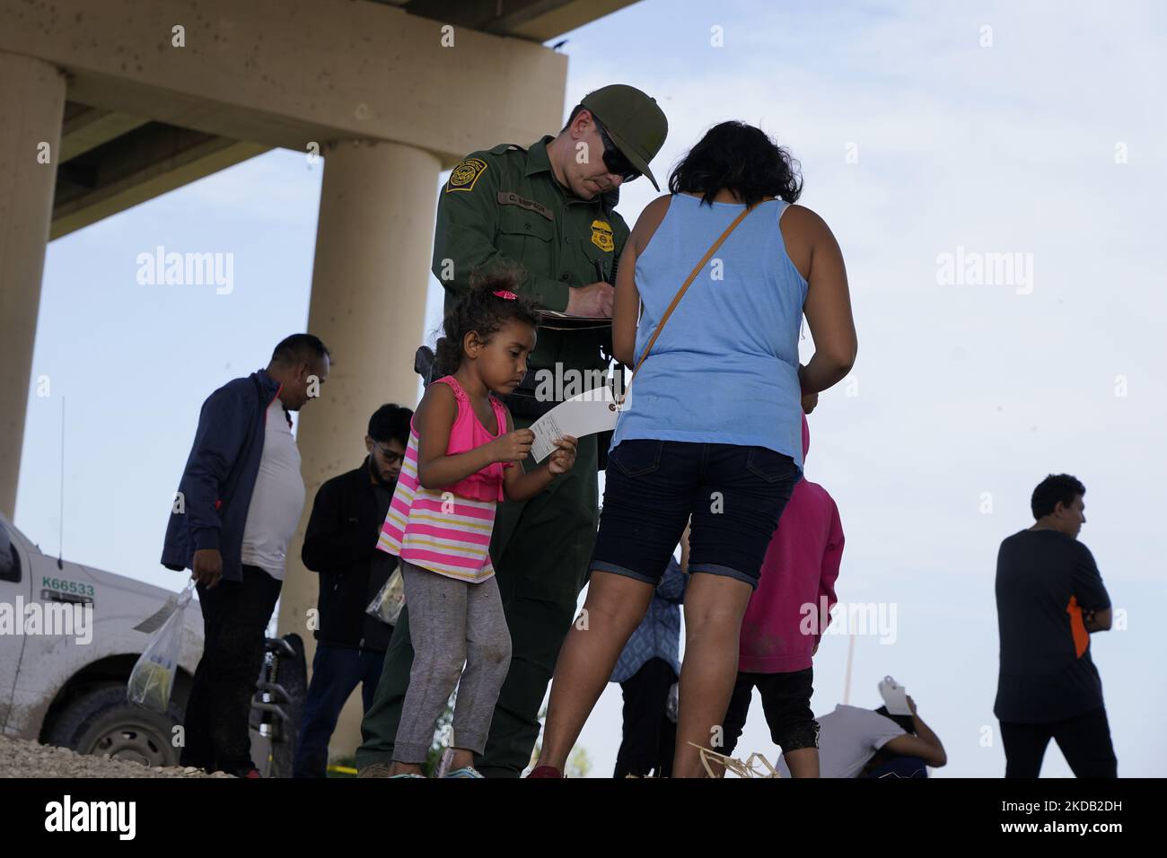 A little girl looks at her mothers identification tag issued by Border Patrol after having crossed the Rio Grande on May 27 2022 in Eagle Pass Texas, USA. Title 42, the Trump era mandate which was set to prevent migrants from entering the US, was to expire on May 23 but was blocked by a lawsuit filed by several states citing that the move to strike down the law “failed to meet standards set by the Administrative Procedure Act” and that there is no permanent solution to handling the inevitable surge in immigration. Opponents to upholding of the law voiced their demands stating that Title 42 is  Stock Photo