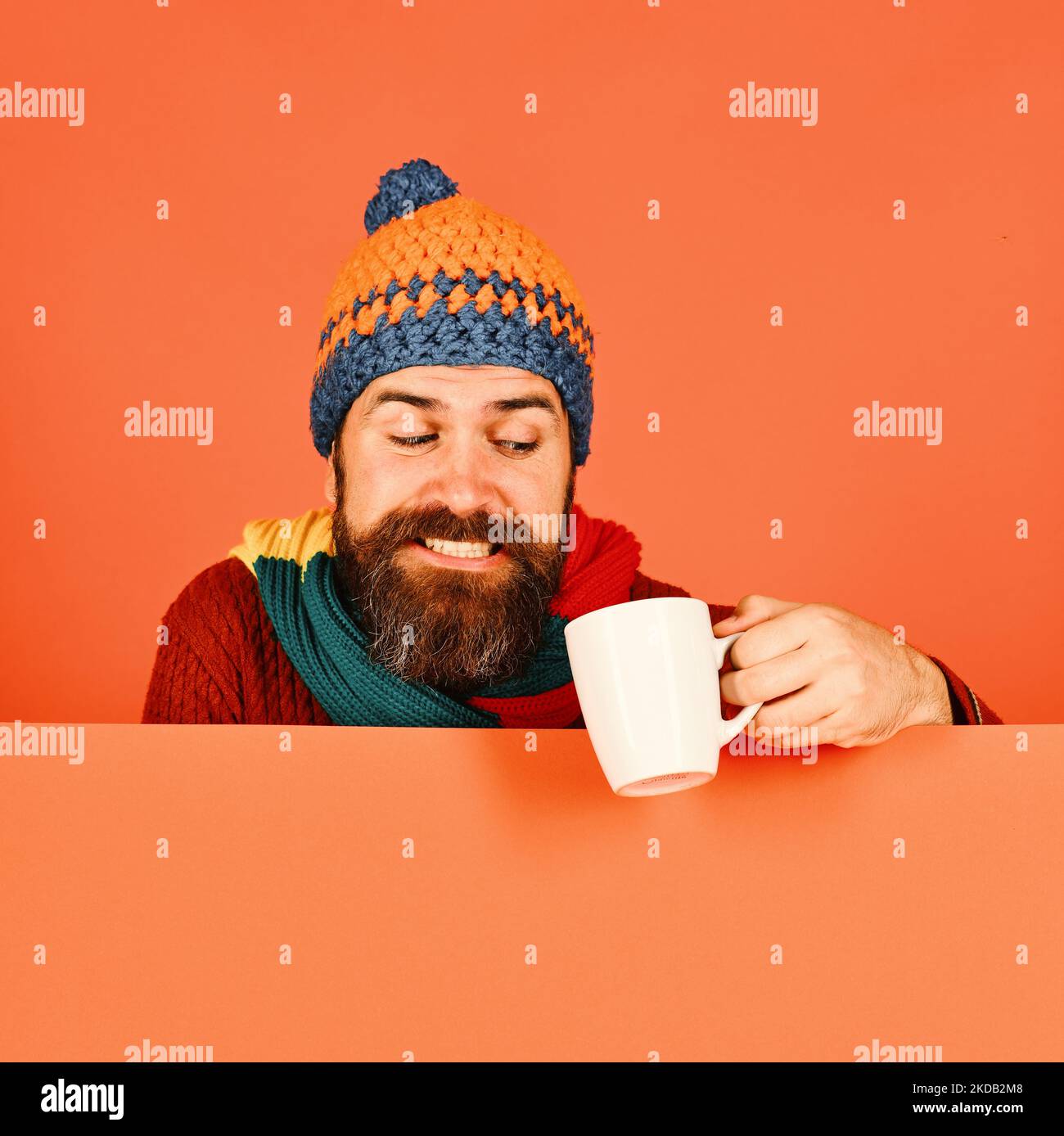 Man in warm hat holds white cup on orange background Stock Photo