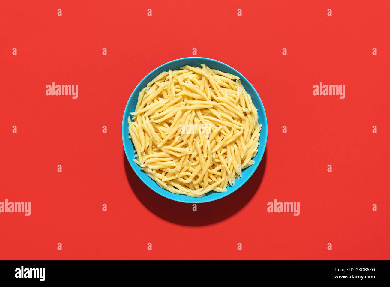 Trofie pasta with no sauce minimalist on a red background. Italian short pasta, called Trofie, in a bowl on a vibrant-colored table. Stock Photo
