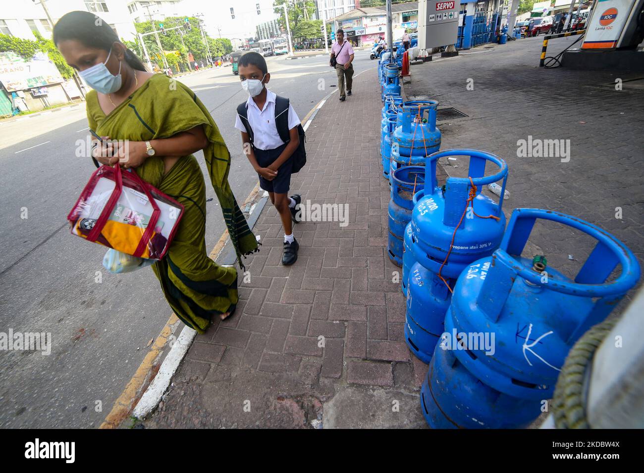 A Sri Lankan mother and son walk across a street filled with chained empty domestic gas cylinders kept in front of a deserted gas station that is closed due to lack of fuel and gas stocks at Colombo, Sri Lanka. 10 June 2022. (Photo by Tharaka Basnayaka/NurPhoto) Stock Photo